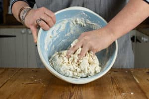 Person holding bowl and bringing together slow cooker bread dough in it with their hands