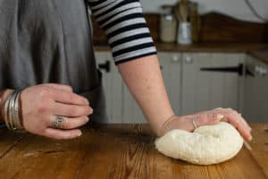 Person kneading slow cooker bread dough with their hand on a wooden surface