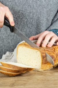 Loaf of slow cooker bread being sliced by a person holding a knife