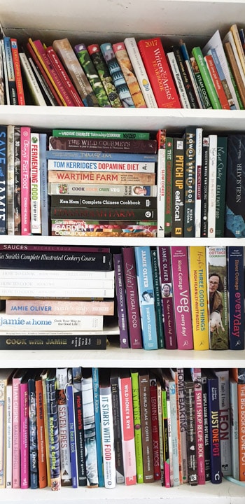 4 shelves of a white bookcase stuffed with LOTS of cookbooks!