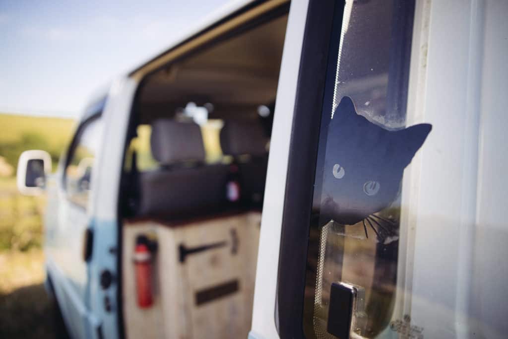 Campervan with sliding door open and a sticker of a silhouette of a black cat stuck in the window