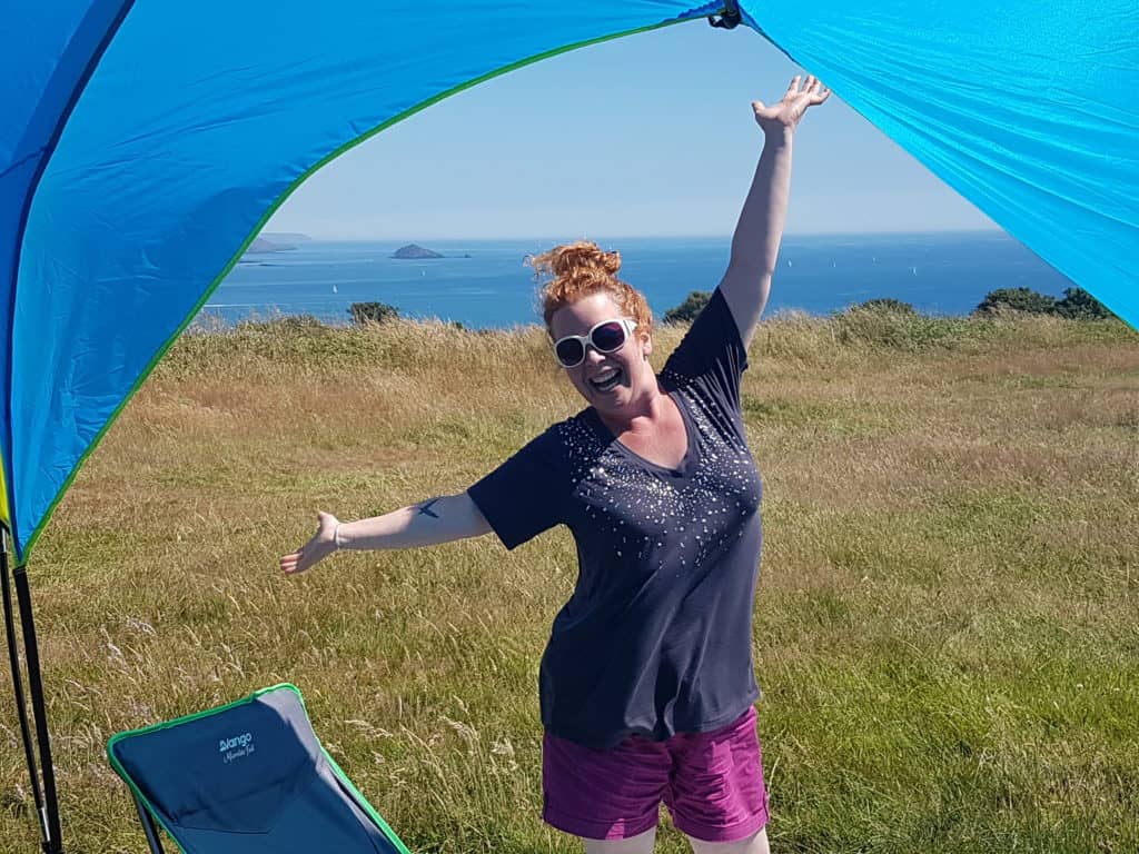 Presenter of Hedgecombers Kitchen stood under a canopy in a field with sea behind, looking happy.