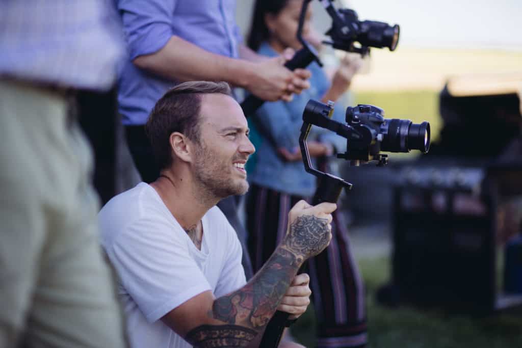 Camera crew holding cameras, focused on one man crouched down