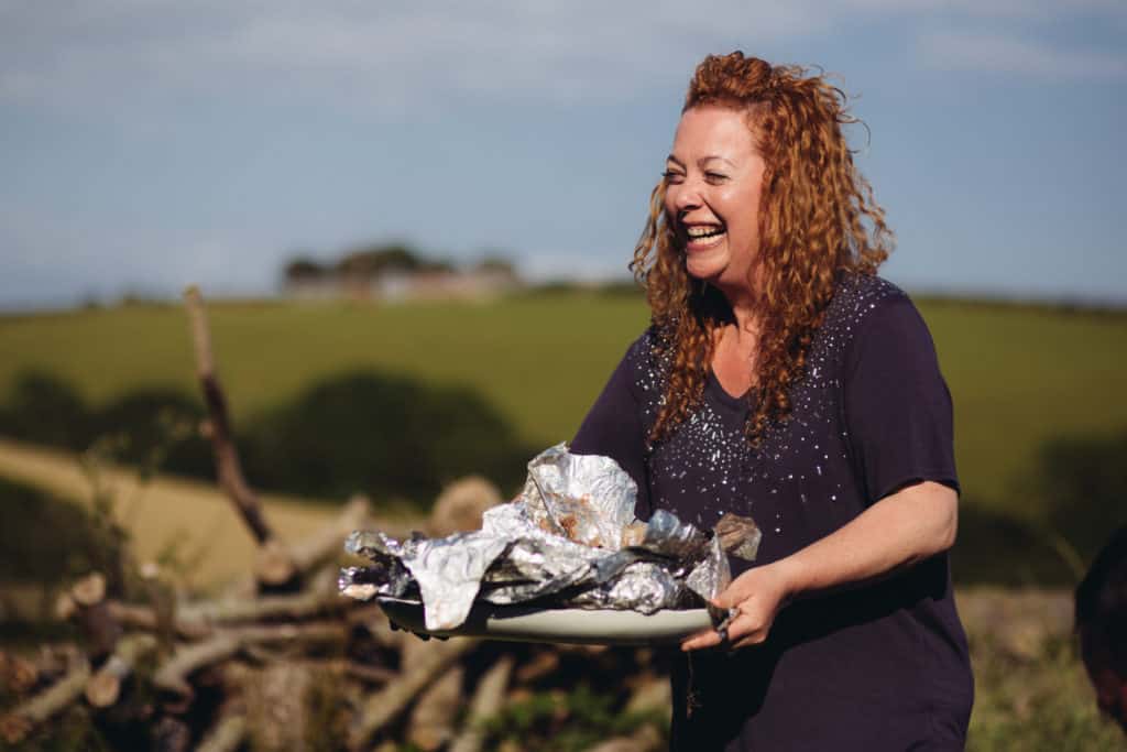 Laughing Hedgecombers Kitchen presenter holding plate of food wrapped in foil outdoors