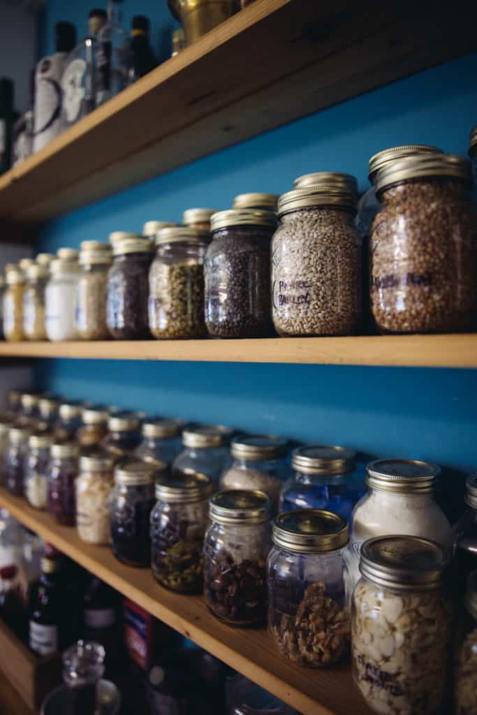 Wooden shelves containing lots of herbs, spices and ingredients stored in small glass jars 