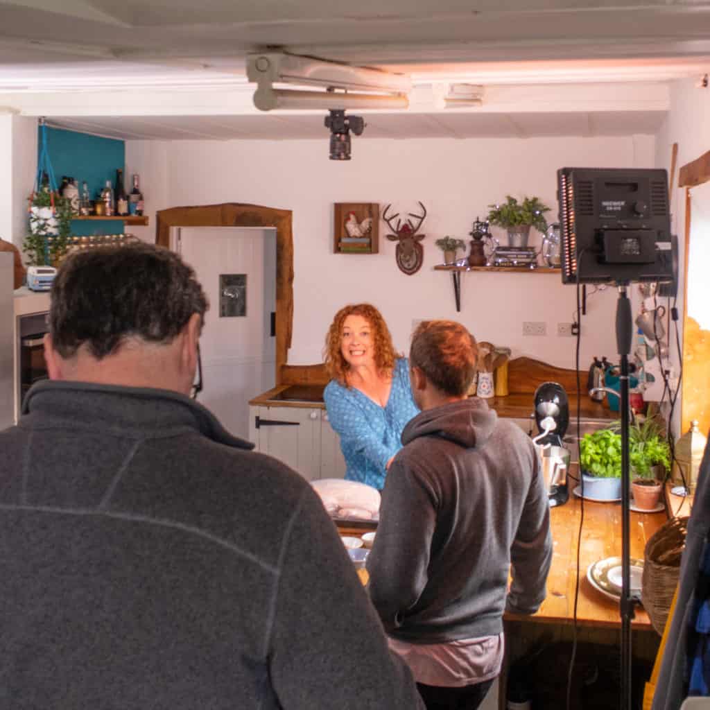 Woman smiling at the camera in a kitchen with backs of two men to camera