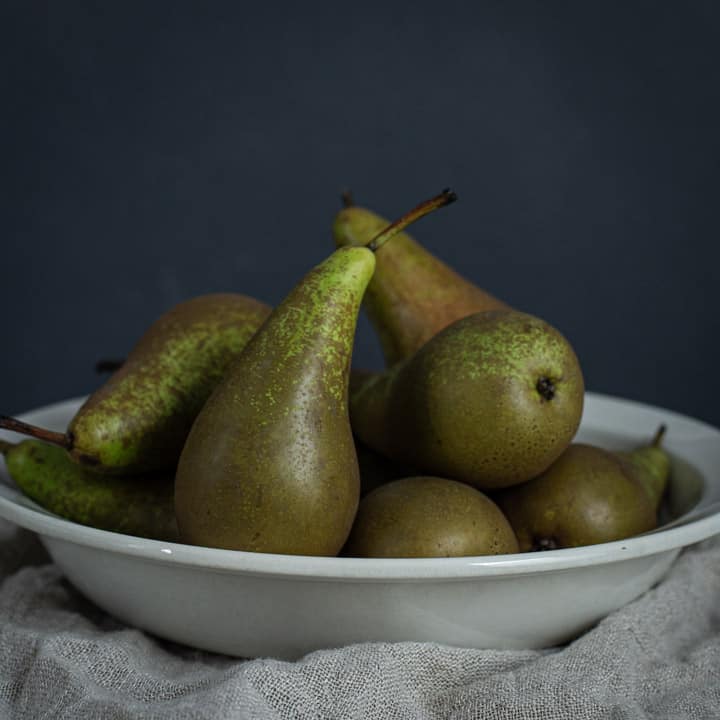 white bowl filled with several pears against a black background