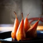 hot poached pears cooling on a blue plate with steam rising in the background