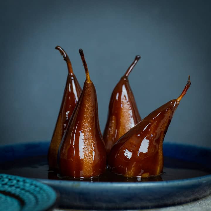 poached pears in spiced prune juice standing on blue plate