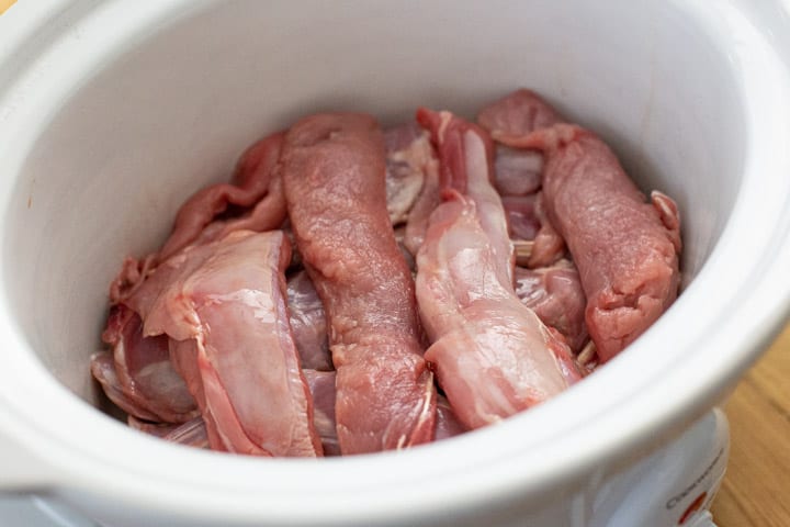 white slow cooker bowl with rabbits joints inside ready for cooking