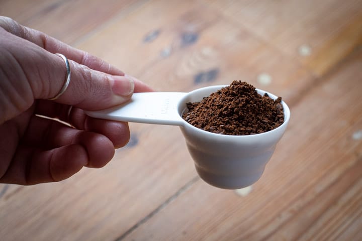 white coffee scoop full of ground coffee against a wooden background