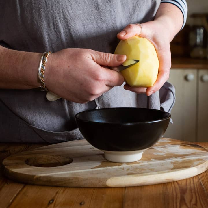 womans hands chipping a raw potato for making a pasty