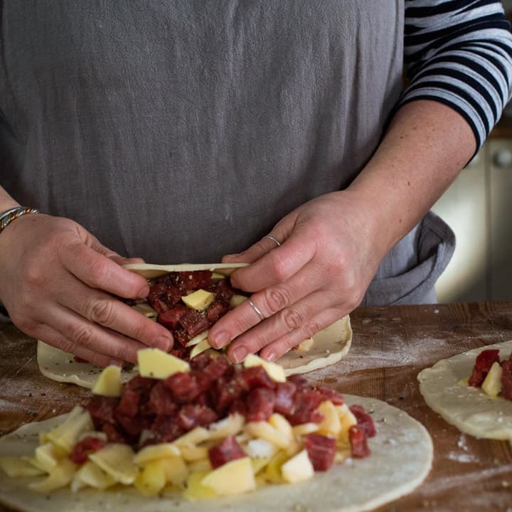 womans hands folding pastry over pasty fillings read to crimp