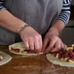 womans hands making three Cornish pasties on a wooden kitchen counter