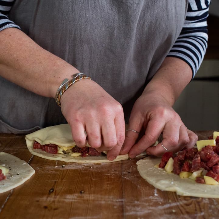 womans hands making three Cornish pasties on a wooden kitchen counter