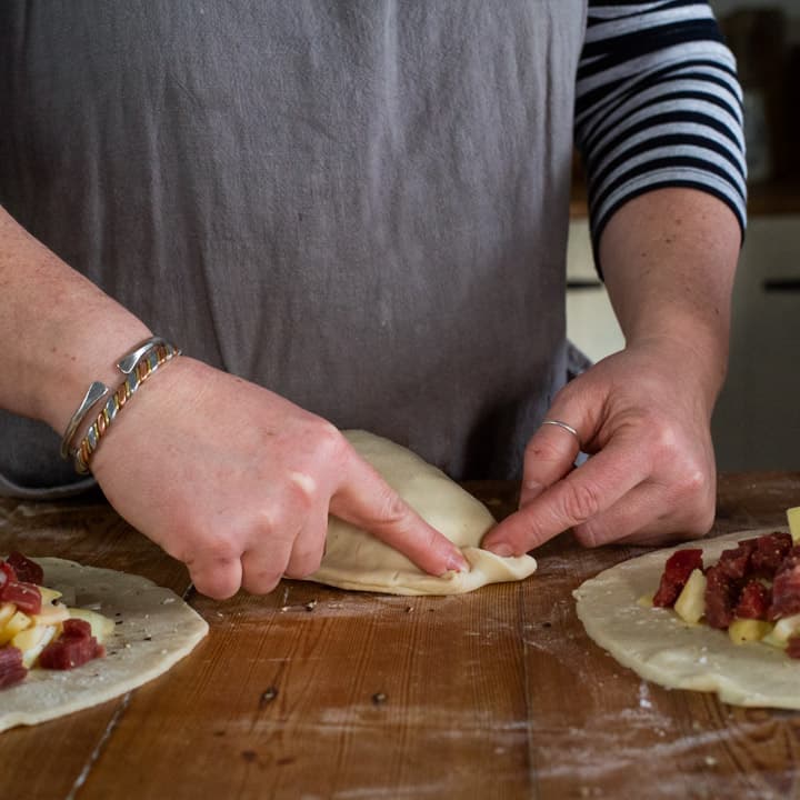 womans hands making a Cornish pasty on a wooden counter