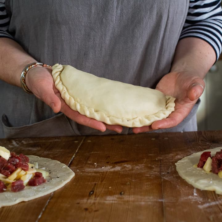 womans hands holding an uncooked, homemade pasty that is ready to be baked