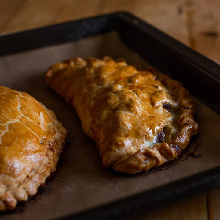 golden brown baked pasty's on brown baking paper on a black tray