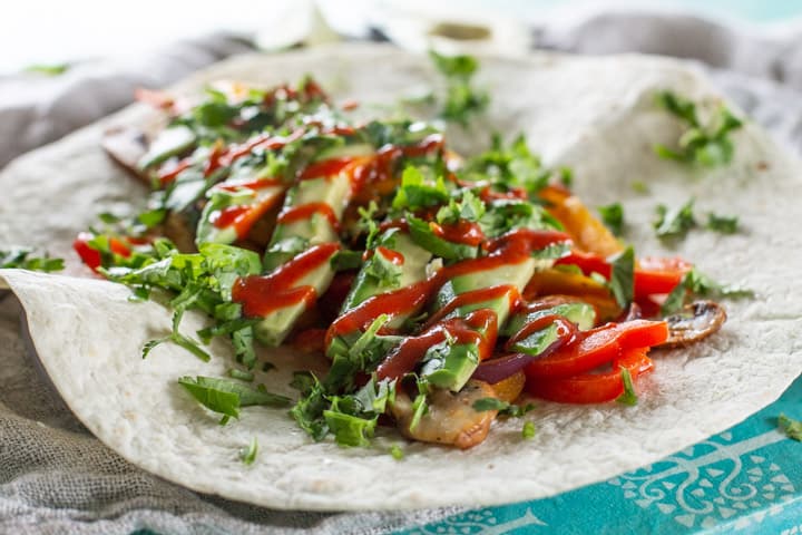 white tortilla wrap with vegetarian fajitas topped with avocado, hot sauce and coriander