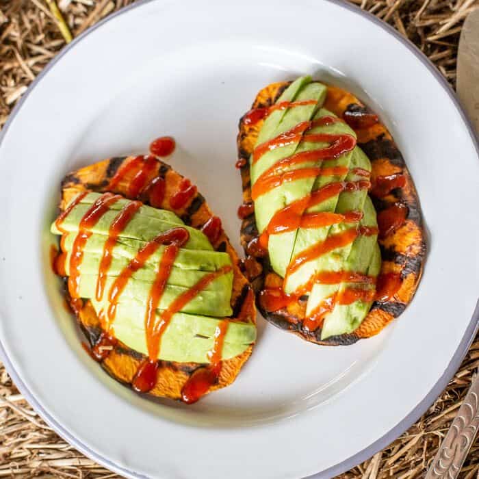 white plate with sweet potato toast, avocado and red hot sauce