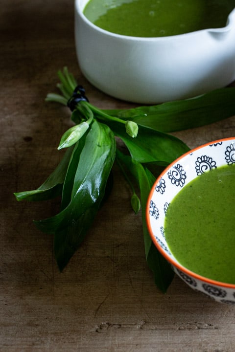 small bunch of wild garlic leaves next to a bowl of bright green wild garlic soup