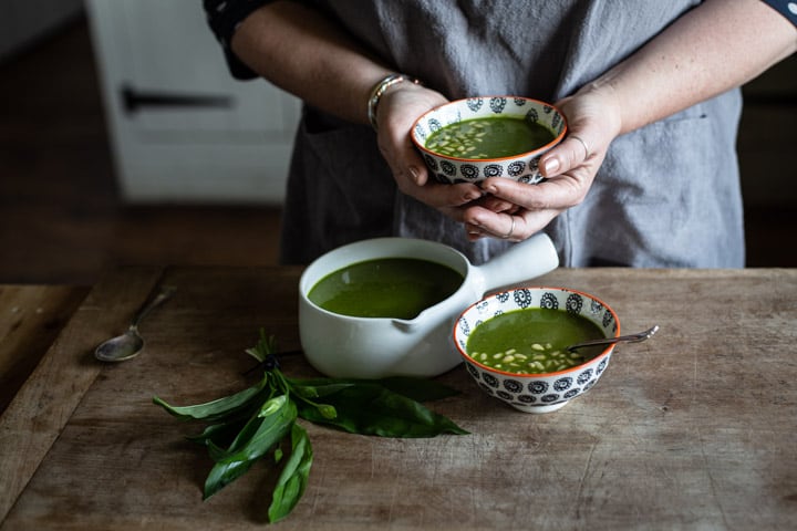 womans hands holding a small bowl of bright green wild garlic soup