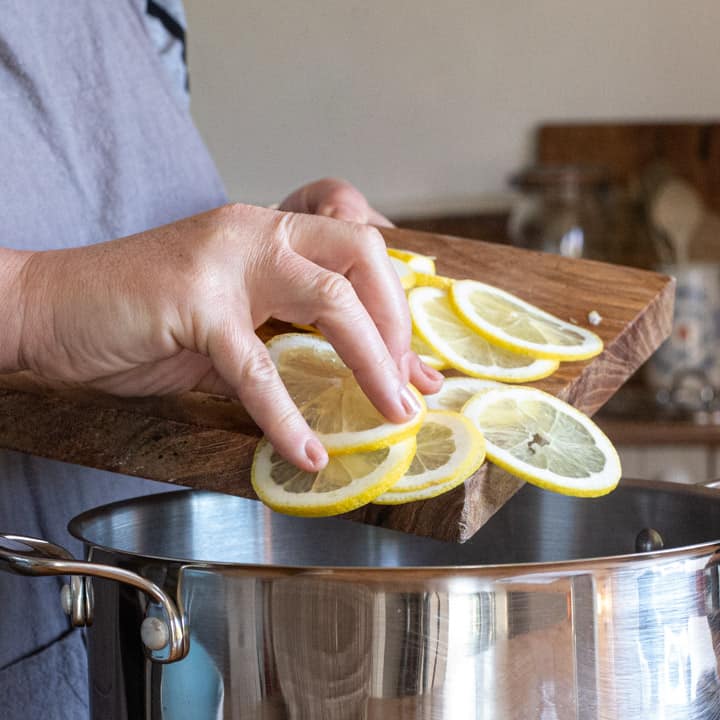 woman in grey tipping slices of lemons form a wooden board into a silver saucepan