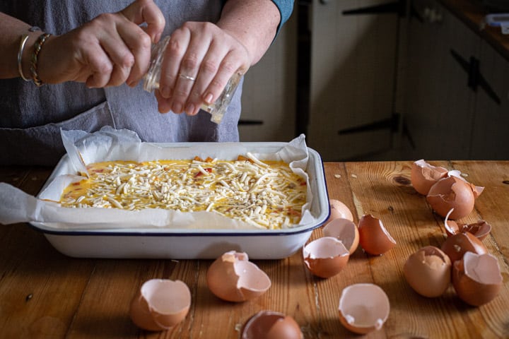 womans hands grinding black pepper over a chorizo and sweet potato frittata