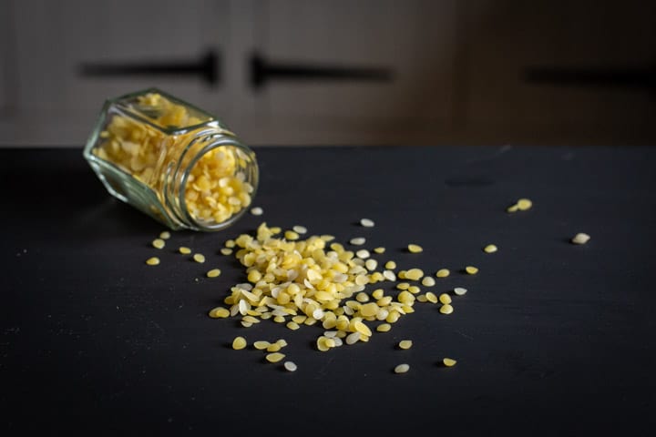 black background with a small glass jar on its side spilling small beeswax beads