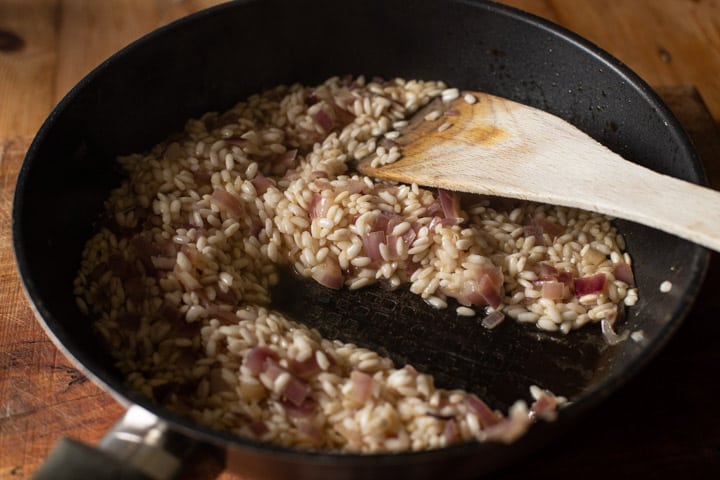 a black skillet with risooto rice and onion gently cooking and a wooden spatula