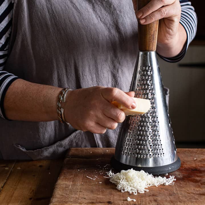 womans hands grating parmesan cheese with a tall cone shaped cheese grater