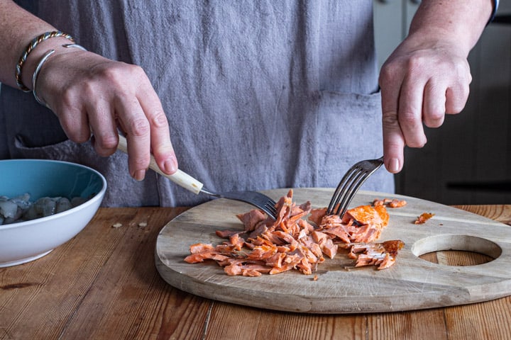 womans hand holding two forks shredding a salmon fillet into flakes