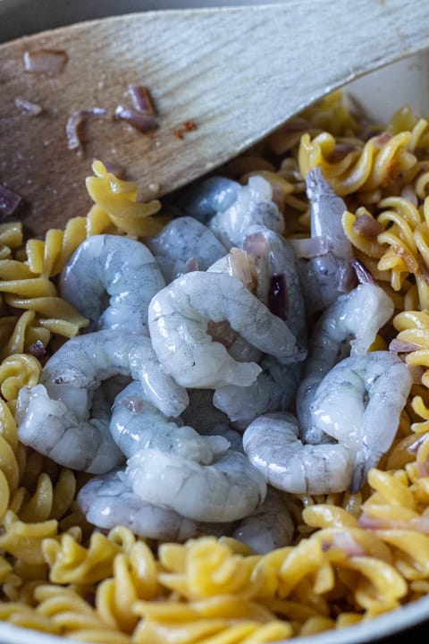 close up of raw grey prawns in a pan of fusilli pasta