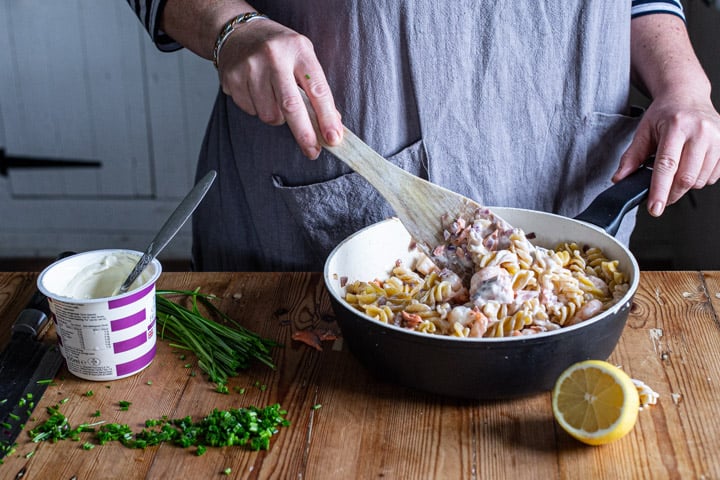 womans hands stirring a pan of salmon and prawn pasta 