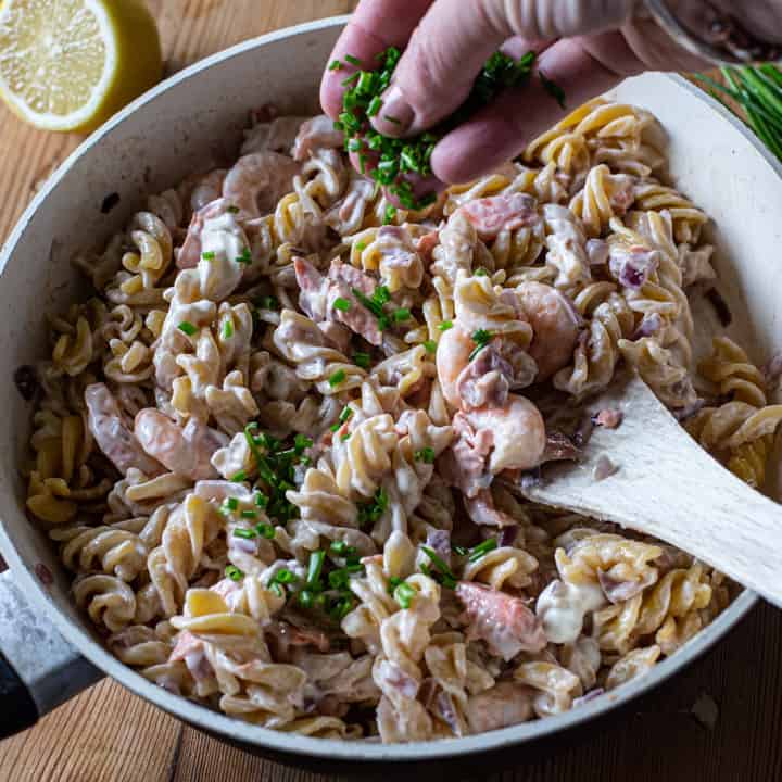 white pan with salmon prawn pasta against a wooden background