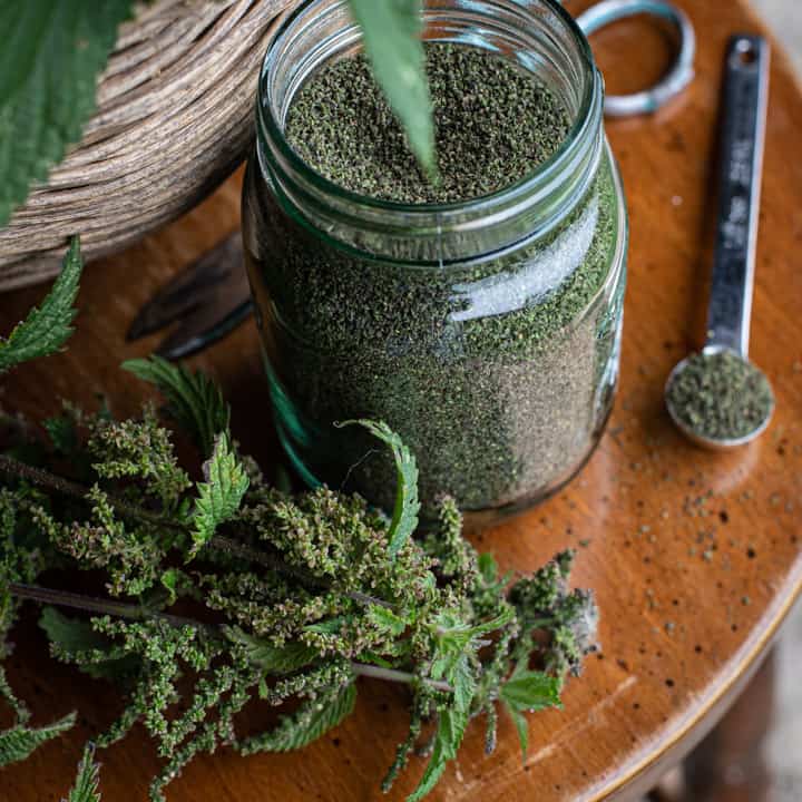 glass jar of nettle seeds, nettle tops and teaspoon of seeds on wooden background