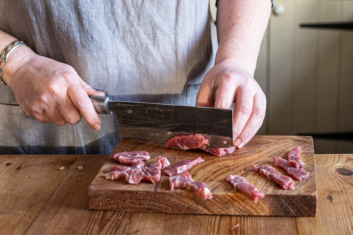 womans hands chopping sirloin steak on a wooden board with large Japanese knife