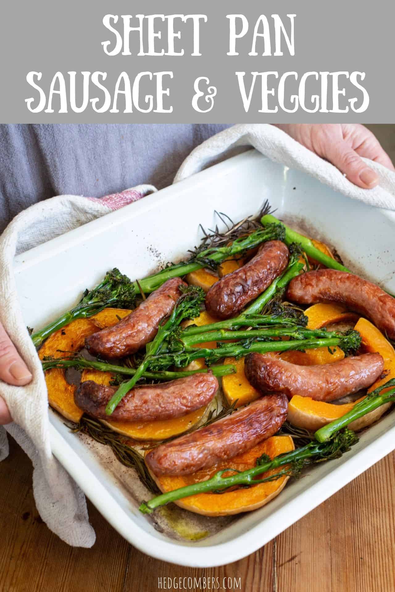 woman in grey holding a white enamel sheet pan with sausages, broccolini and butternut squash