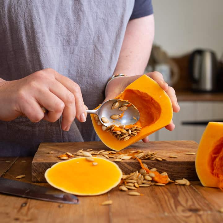 woman in grey scooping seeds out of a halved butternut squash with a silver spoon