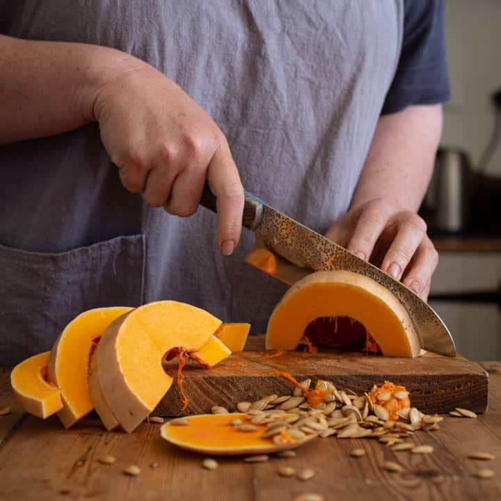 woman in grey slicing a butternut squash on a wooden board