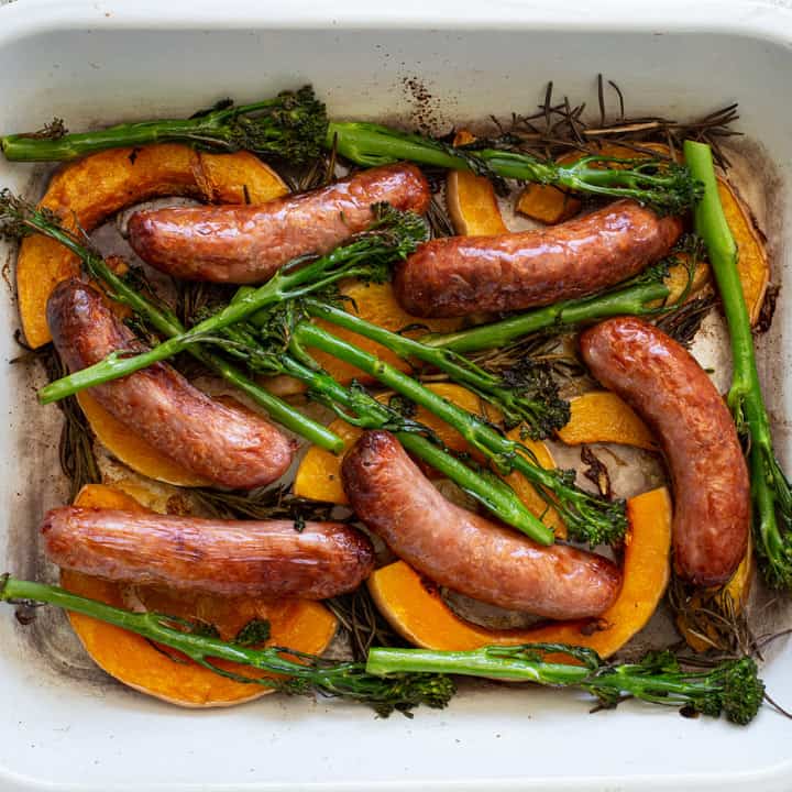 overhead shot of roast sausages and veggies in a white enamel sheet pan dish