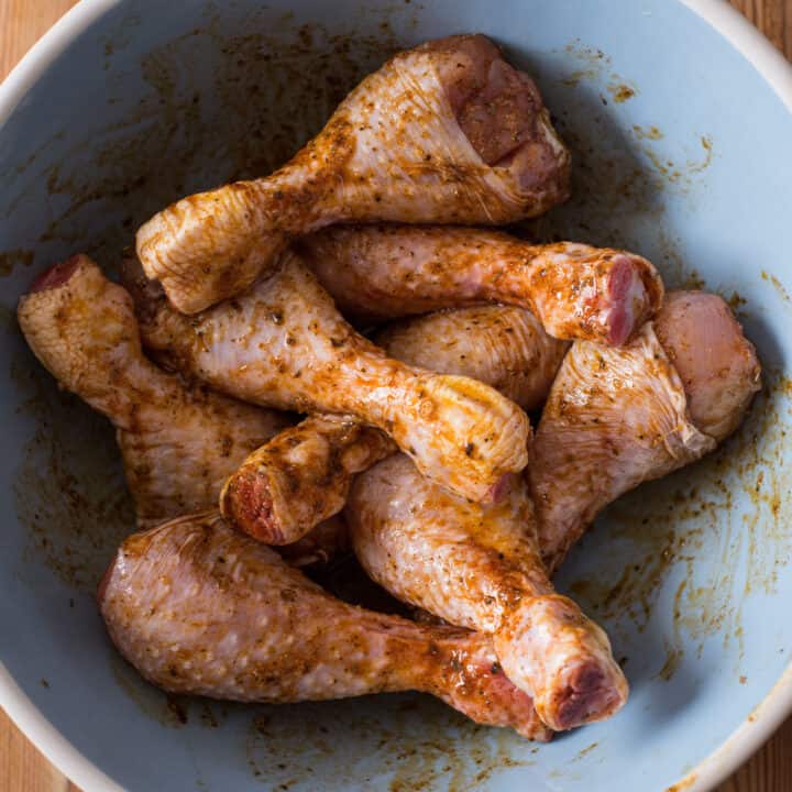 Large blue bowl filled with chicken drumsticks covered in a simple marinade