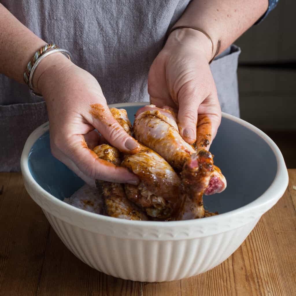 Woman’s hands massaging a homemade marinade into a chicken drumsticks in a large pale blue bowl