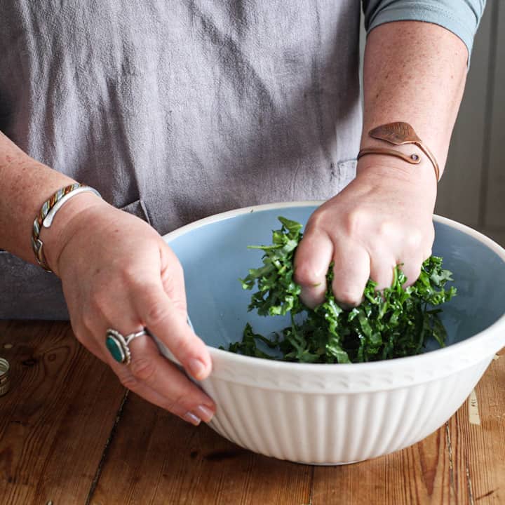Woman’s hands in large blue and white ceramic bowl massaging a handful of bright green kale