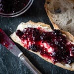 Dark grey piece of slate with 2 slices of fresh sourdough bread topped with home made blackberry jam