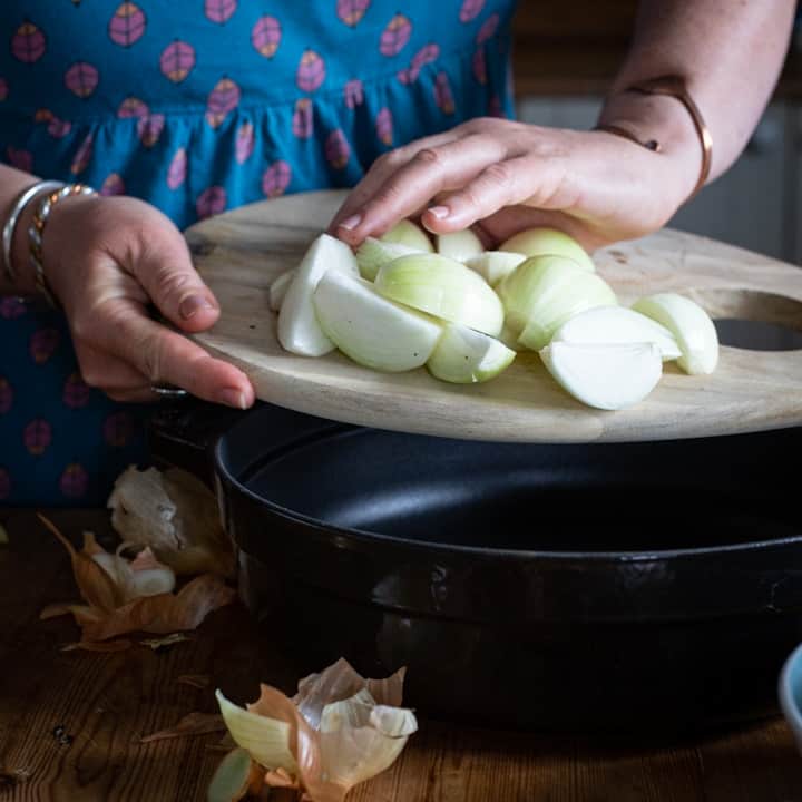 Woman in blue tipping chopped white onions into a black sauté pan