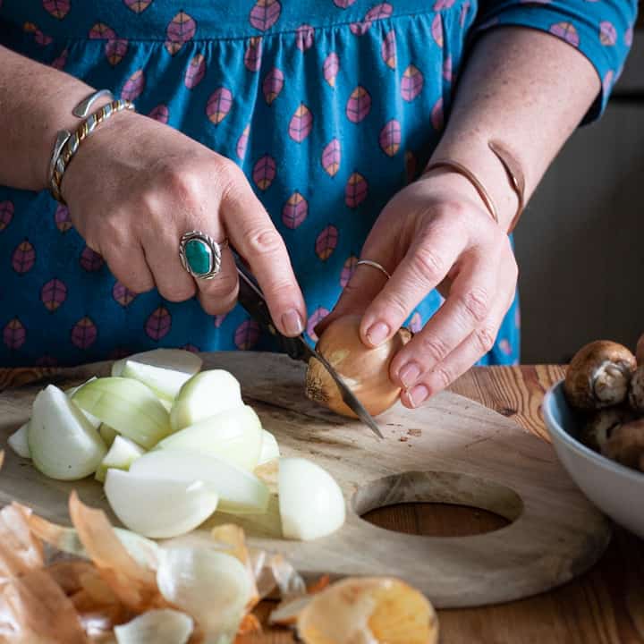 Woman’s hands chopping several white onions on a wooden chopping baord