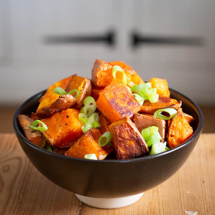 Black bowl piled high with crispy pieces of baked sweet potato and little slices of green spring onion