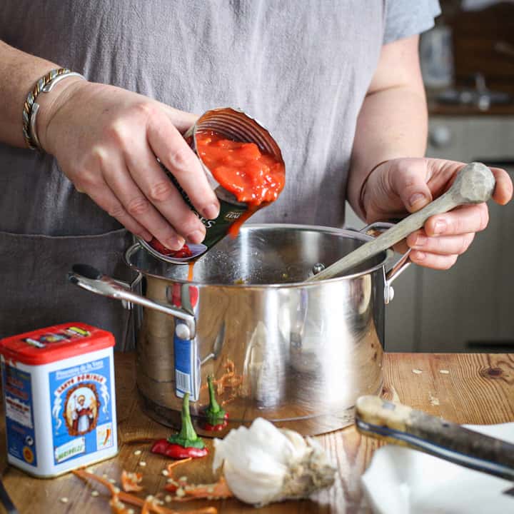 Woman’s hands pouring chopped tomatoes from a can with a black label into a silver saucepan