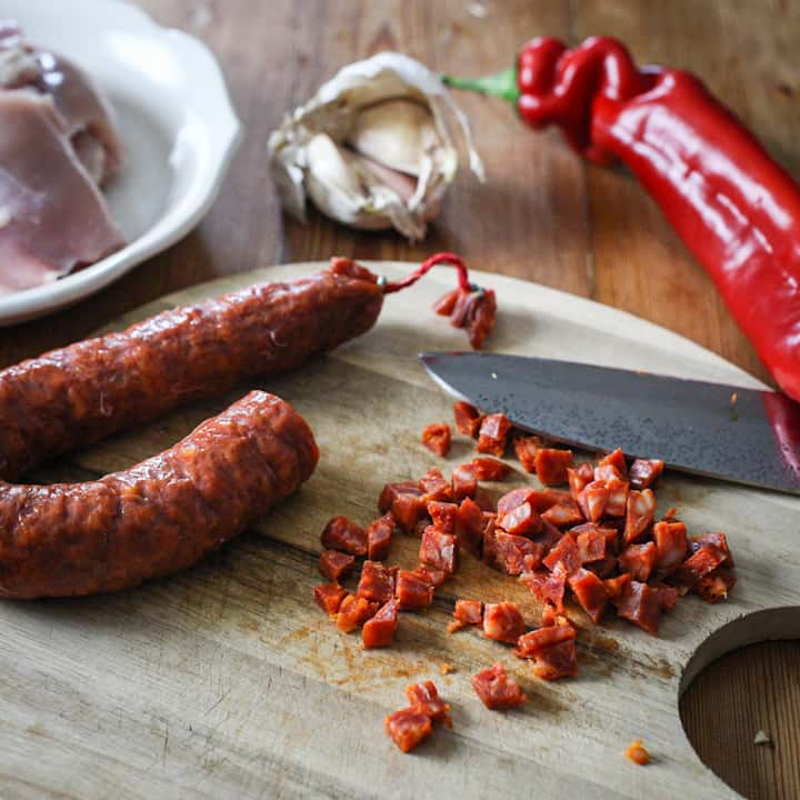 Wooden chopping board with finely diced chorizo, red pepper, garlic and chicken thighs